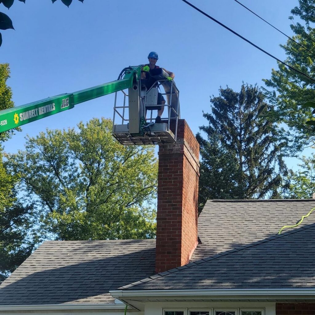 A worker in a lift bucket performing chimney repair or maintenance on a residential chimney by Century Chimney Sweep and Repair in Cleveland, OH