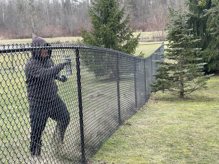 A worker installing a black chain-link fence in a residential or commercial property by STILL Fencing in Rochester, NY.