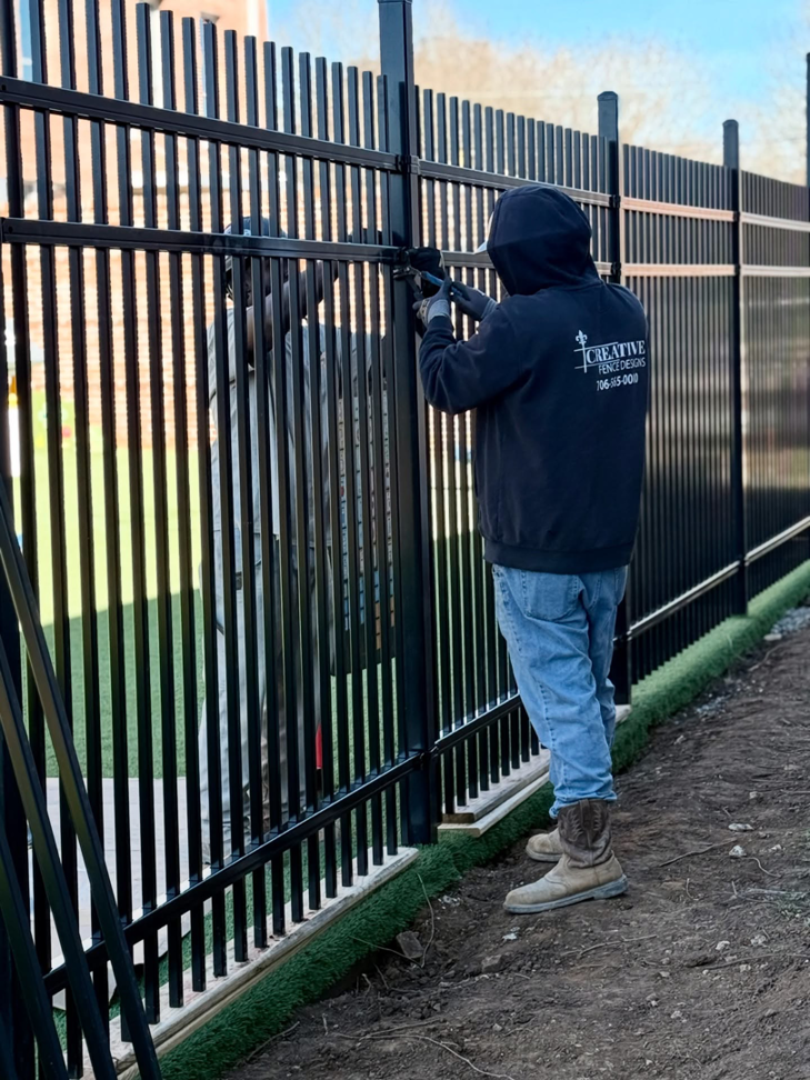 A worker installing a black metal fence for Creative Fence Designs in Columbus, GA.