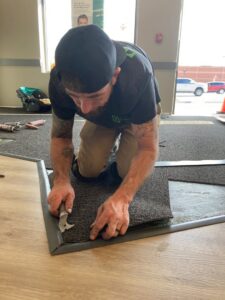 A worker installing carpet tiles at a commercial entrance for Innovative Installations LLC in Rapid City, SD.