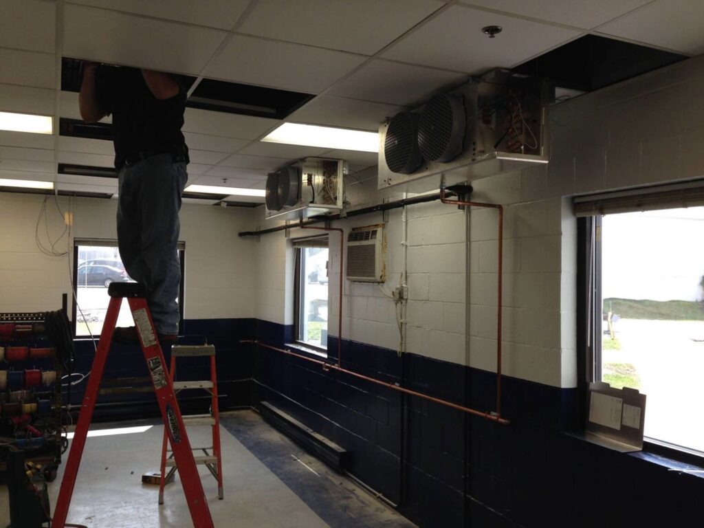 A worker installing ceiling-mounted HVAC units in a commercial space for Accurate Air in Manchester, NH