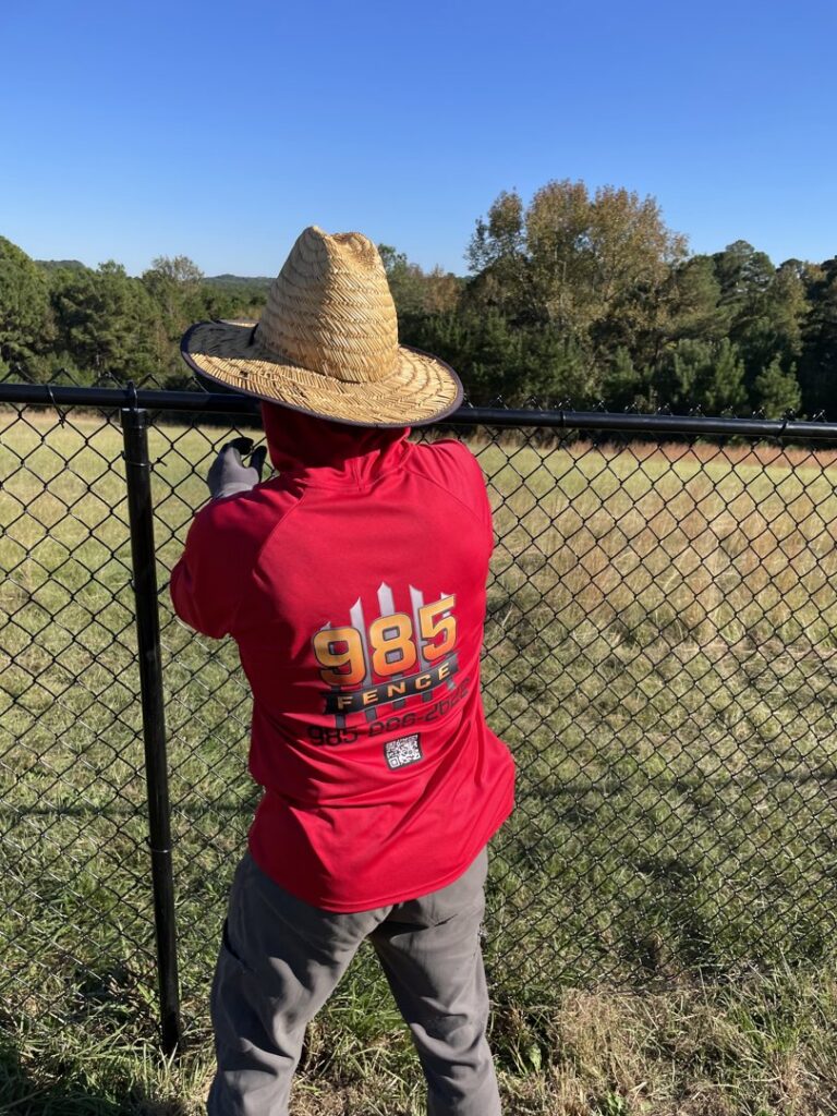 A fencing contractor from 985 Fence, LLC installing a black chain-link fence in Schriever, LA.