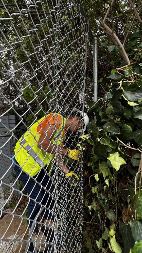 A close-up of a worker installing a chain-link fence, showcasing the work of San Diego Fencing Contractor A's Pro Build Fencing in San Diego, CA.