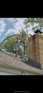 A worker on a roof installing a flexible chimney liner into a brick chimney, performed by Harry's Quality Chimney Services in Kansas City, MO