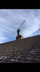 A worker on a roof installing a flexible metal chimney liner, demonstrating a chimney sweep service by Colombus Chimney in Elizabeth, NJ.