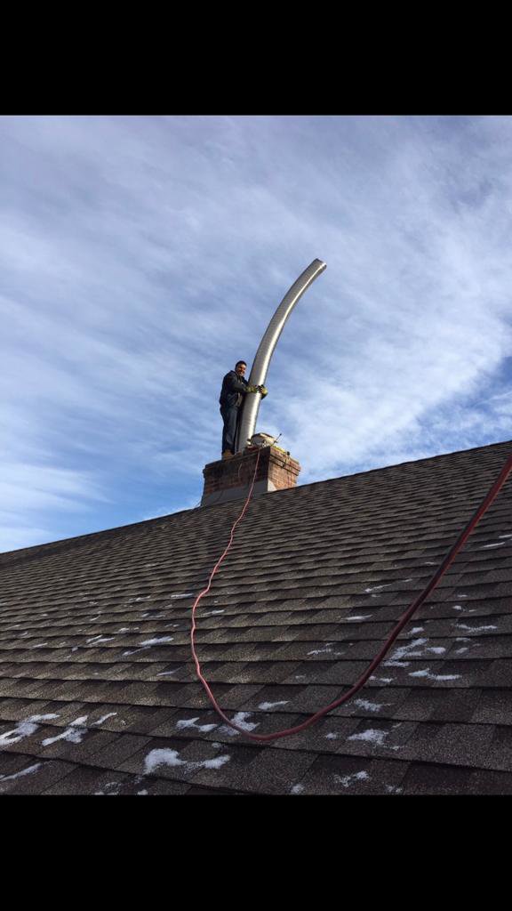 A worker on a roof installing a flexible metal chimney liner, demonstrating a chimney sweep service by Colombus Chimney in Elizabeth, NJ.
