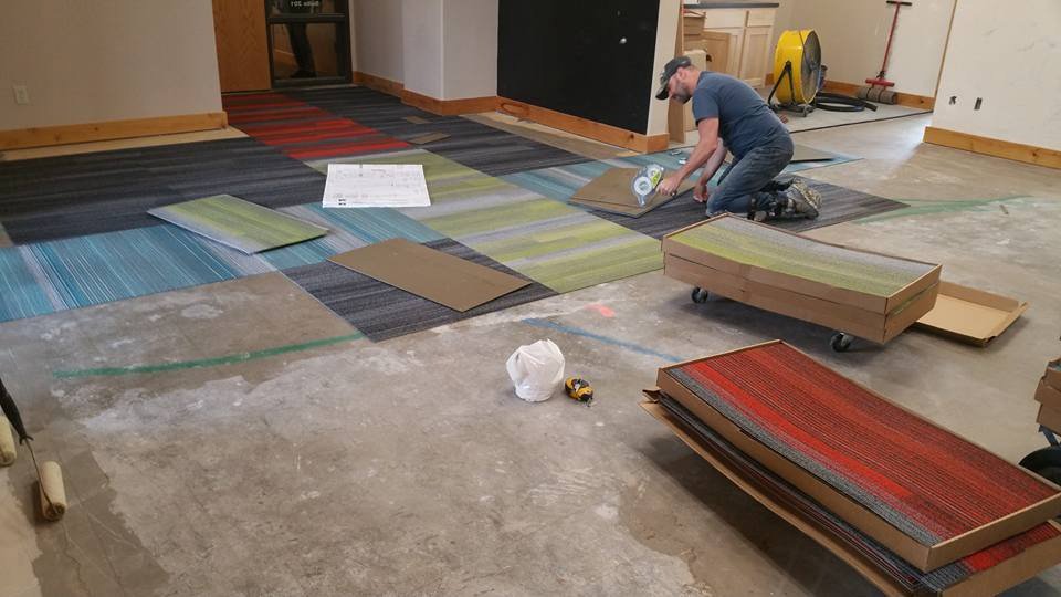 A worker installing colorful carpet tiles in a commercial space for Bozeman Flooring in Bozeman, MT.