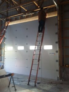 A worker on a ladder installing a commercial garage door for Universal Overhead And Garage Doors in Baltimore, MD.