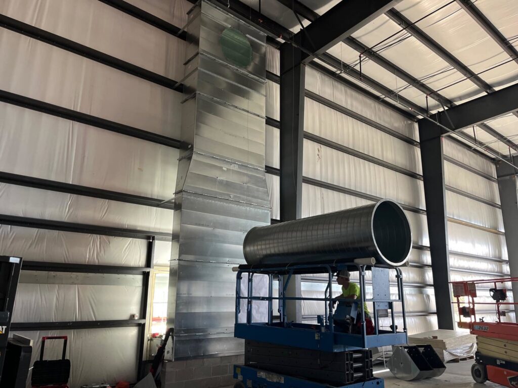 A worker from STAR Heating Cooling Plumbing installing large commercial HVAC ductwork from a scissor lift in Fishers, IN.