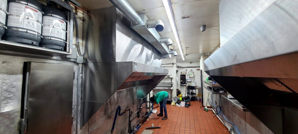 A worker installing commercial kitchen ventilation with stainless steel hoods and ductwork for Butte Tin Shop, Inc. in Butte, MT.