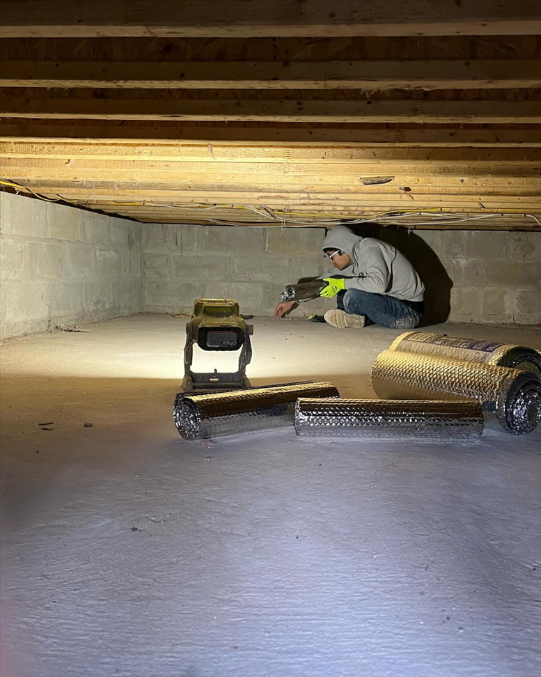 A worker installing insulation in a crawl space for Liquid Green Spray Foam Insulation in Brewster, NY