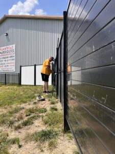 A worker installing a fence panel at a commercial site, demonstrating work by Sol Fence LLC in Evansville, IN.