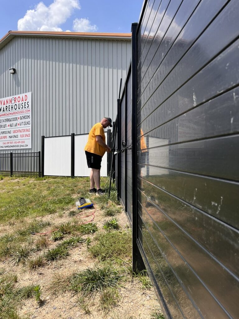 A worker installing a fence panel at a commercial site, demonstrating work by Sol Fence LLC in Evansville, IN.
