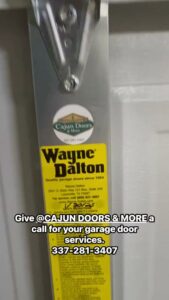 A worker on a ladder installing a garage door opener in a residential garage, demonstrating service by Cajun Doors & More in Lafayette, LA.