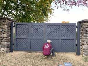 A worker installing a dark grey wooden gate between stone pillars for RP Fencing & Gates in Brewster, NY
