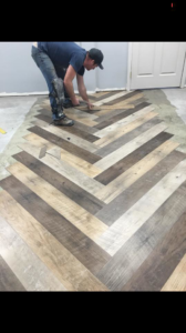 A worker installing herringbone pattern luxury vinyl plank flooring for McCulloch Commercial Flooring in Fairbanks, AK