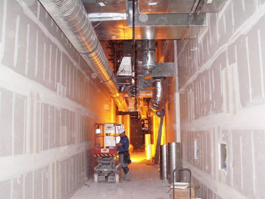 A worker on a scissor lift installing HVAC ductwork in a commercial hallway for 1st Team Air Conditioning in Anaheim, CA