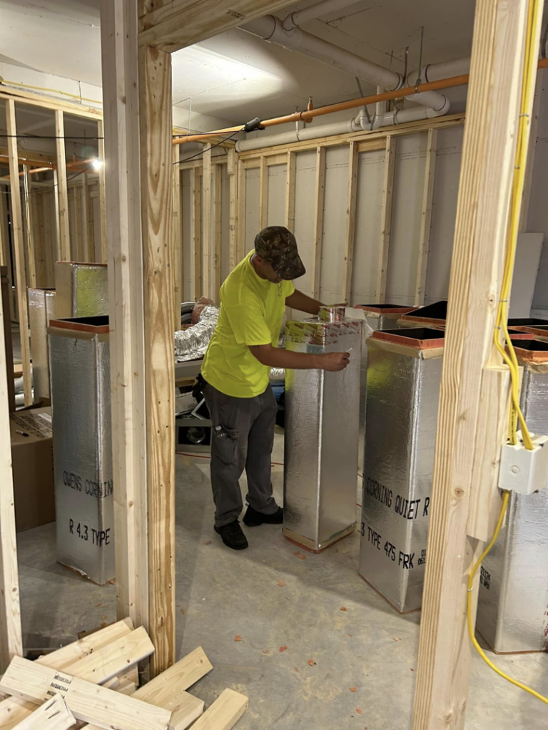 A worker installing insulated HVAC ductwork in a new construction project by HP Mechanical LLC in Santa Rosa, CA.