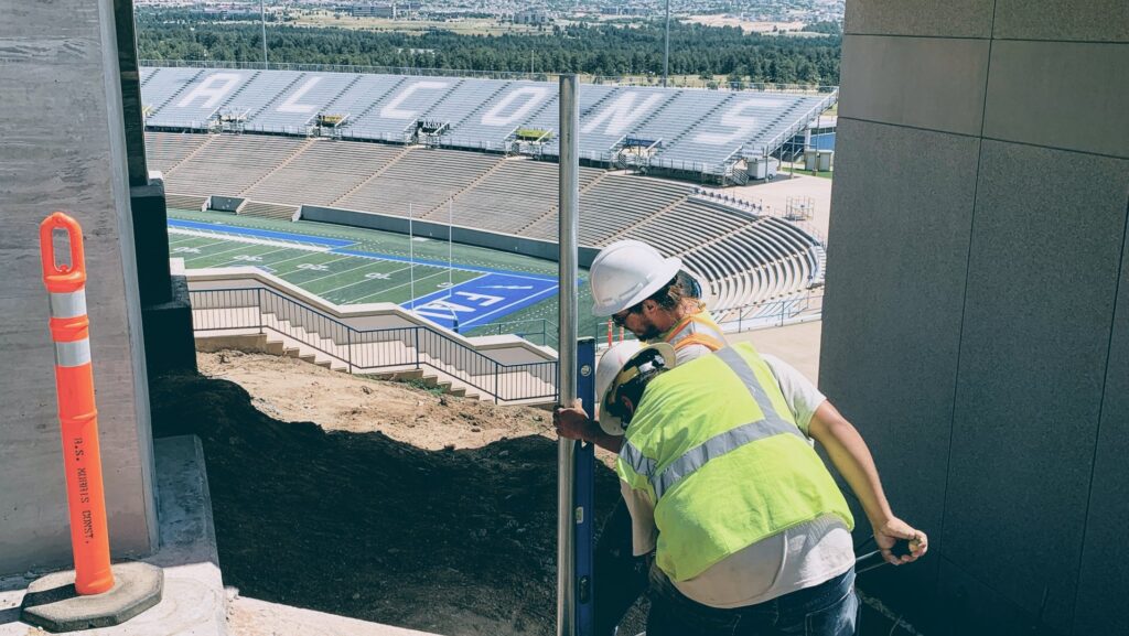 A worker installing a metal fence post near a stadium, demonstrating work by Colorado Springs Fence Company in Colorado Springs, CO.