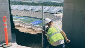 A worker installing a metal fence post near a stadium, demonstrating work by Colorado Springs Fence Company in Colorado Springs, CO.