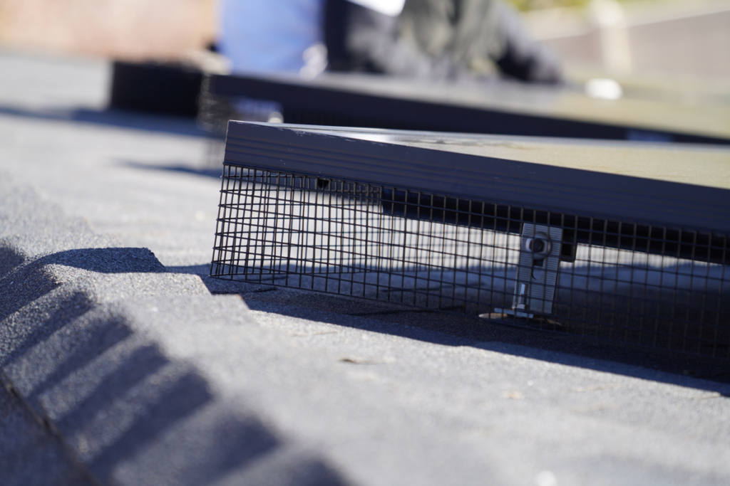 A worker installing protective bird guards around solar panels on a roof by Bell Mountain Solar Panel Bird Guards in Orem, UT