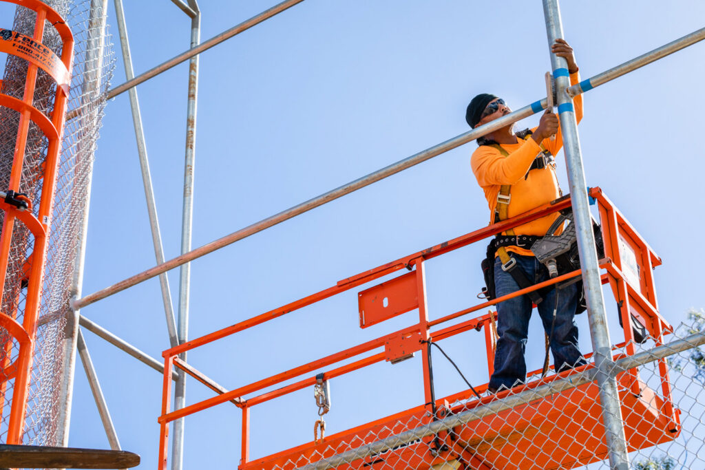 A worker on a lift installing a tall chain-link fence for Upright Fencing Hawaii LLC in Kapolei, HI.