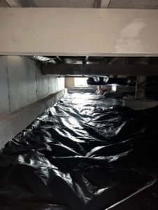 A worker installing a black vapor barrier in a crawl space for moisture control at Buzz Pest Control in Springfield, MO.