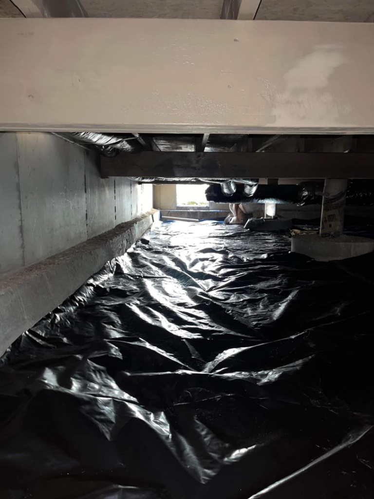 A worker installing a black vapor barrier in a crawl space for moisture control at Buzz Pest Control in Springfield, MO.