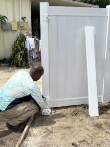 A worker installing hinges on a white vinyl fence gate for Santis Fence & Home Service in Tampa Heights, FL