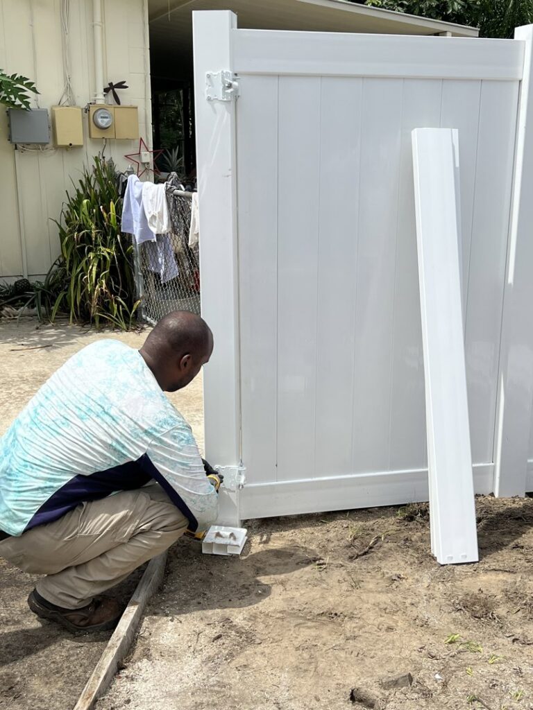 A worker installing hinges on a white vinyl fence gate for Santis Fence & Home Service in Tampa Heights, FL