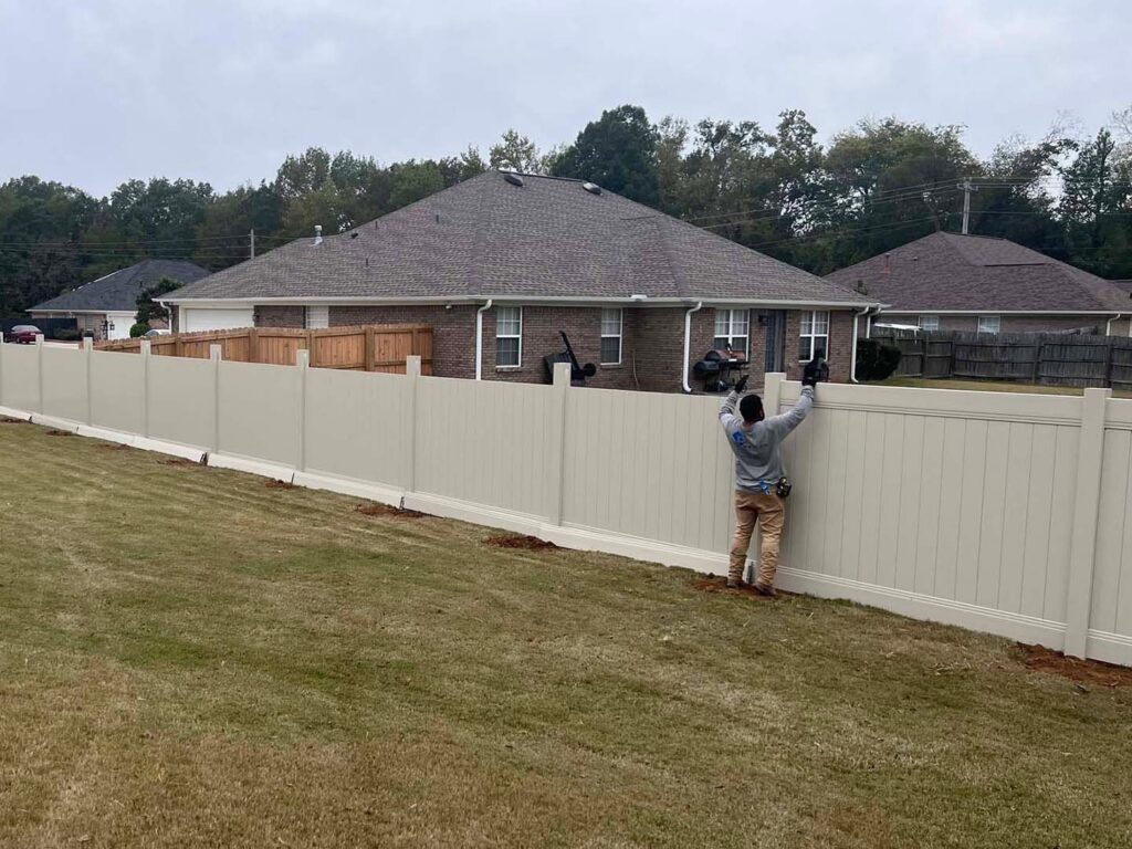 A RUCO Fence contractor installing a beige vinyl privacy fence in a residential backyard in Huntsville, AL.