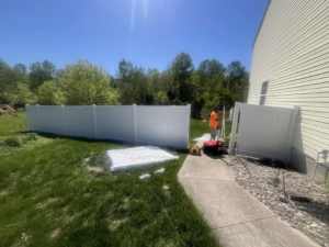 A worker installing a white vinyl privacy fence in a sunny backyard for Fence Pros LLC in Medford, OR.