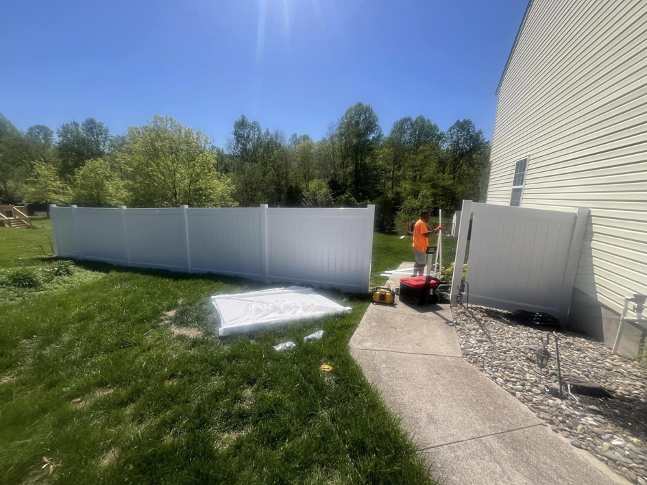 A worker installing a white vinyl privacy fence in a sunny backyard for Fence Pros LLC in Medford, OR.