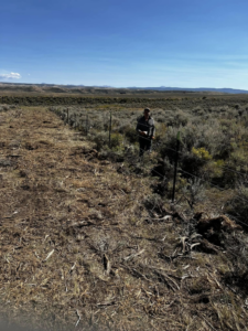 A worker installing a wire fence in an open field for Tomahawk Fencing in Riverton, WY.