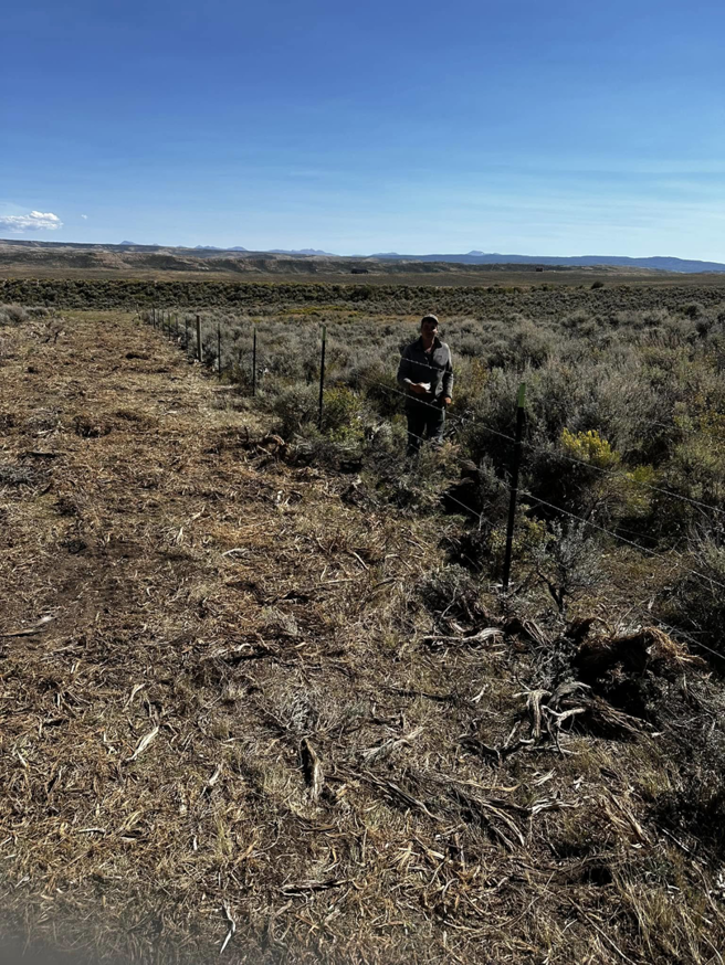 A worker installing a wire fence in an open field for Tomahawk Fencing in Riverton, WY.