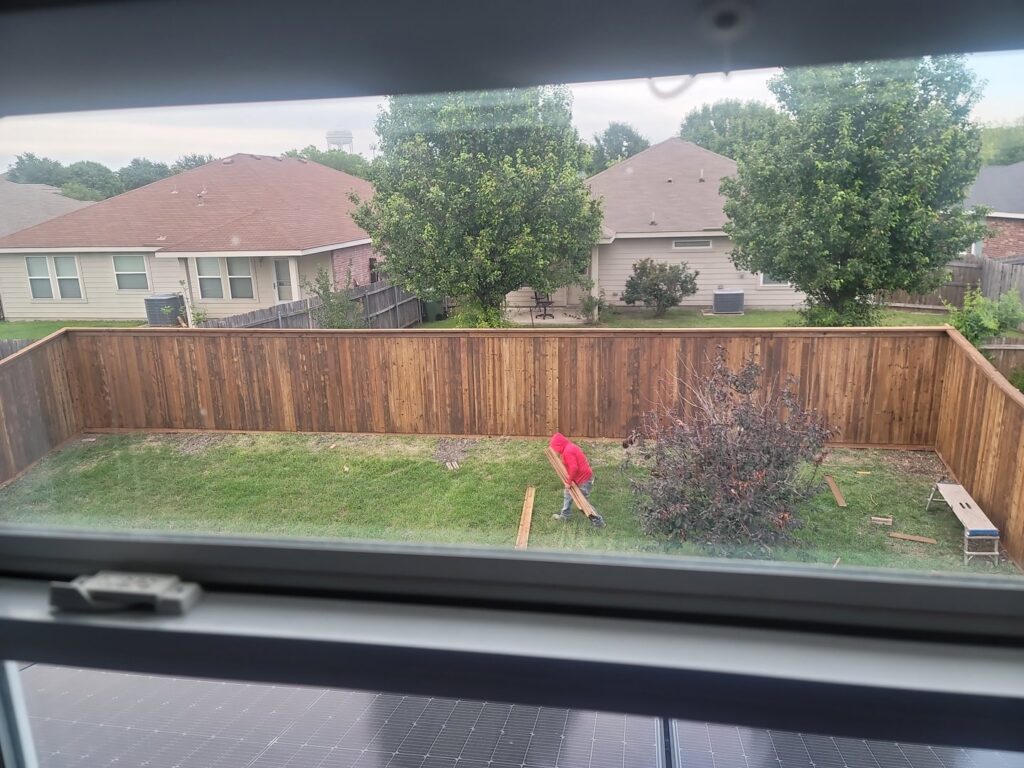A worker installing a new wood fence in a residential backyard, seen from above, by EverFence in Dallas, TX.