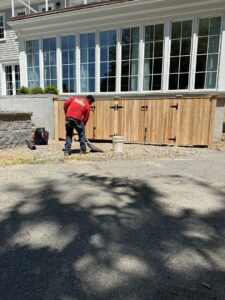 A worker shoveling dirt during the installation of a wooden fence structure by New England landscaping and fence inc in Lynn, MA.