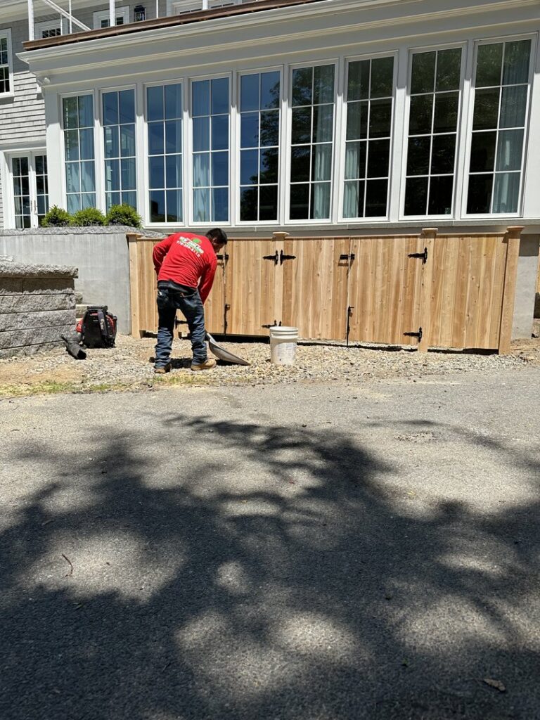 A worker shoveling dirt during the installation of a wooden fence structure by New England landscaping and fence inc in Lynn, MA.