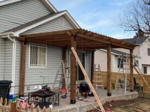 A worker installing a custom wooden pergola over a patio, a service offered by R&S Fencing & Design LLC in Denver, CO.