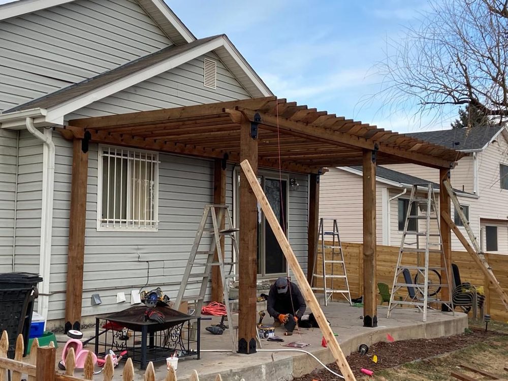 A worker installing a custom wooden pergola over a patio, a service offered by R&S Fencing & Design LLC in Denver, CO.
