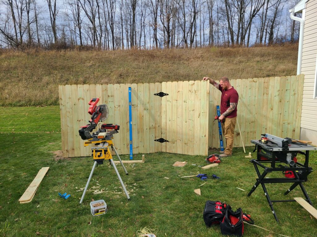 A worker from Camp Carlson Fencing in Rochester, NY, installing a new wood privacy fence with tools on site.