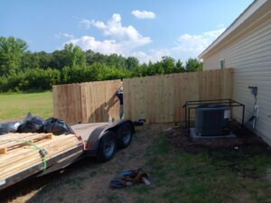 A worker installing a new wood privacy fence with materials on a trailer for Fayetteville Fence Pros in Fayetteville, NC.