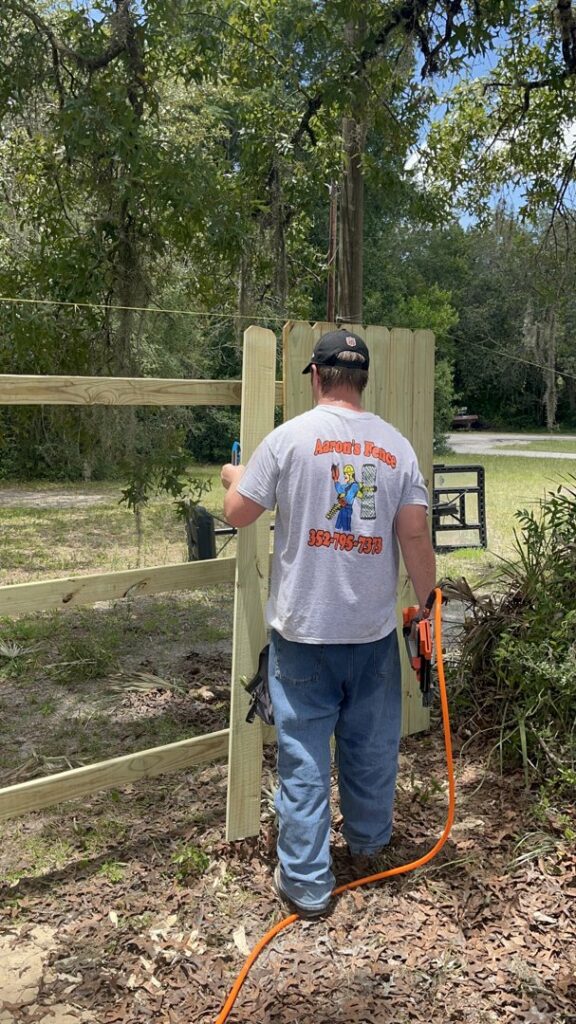 A worker installing wooden fence pickets with a nail gun, wearing an Aarons fence shirt in Homosassa Springs, FL