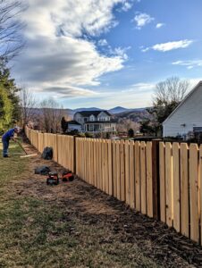 A worker installing a new wooden picket fence in a residential yard for Roanoke Fence Company in Roanoke, VA.