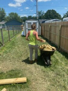 A worker loading wooden fence materials into a wheelbarrow next to a new privacy fence by Stapleton Fencing LLC in Lexington, KY.