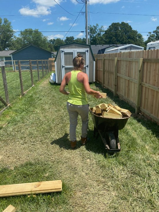 A worker loading wooden fence materials into a wheelbarrow next to a new privacy fence by Stapleton Fencing LLC in Lexington, KY.