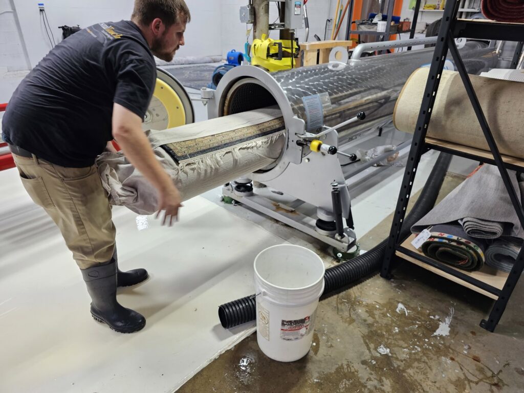 A worker loading a rolled-up area rug into a large automatic cleaning machine at Personal Touch Carpet Cleaning in Chicago, IL.