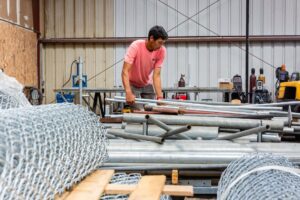 A worker moving metal fence posts and chain link rolls in the warehouse for Upright Fencing Hawaii LLC in Kapolei, HI.