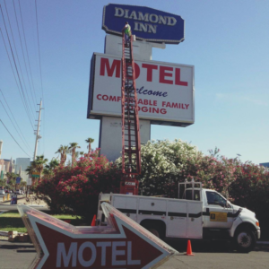 A worker on a tall ladder repairing a motel sign with a boom truck from Desert Clark County Lighting in Las Vegas, NV.