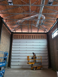 A worker on a yellow scissor lift installing a large commercial garage door for Iconic Garage Door Service in Queen Creek, AZ